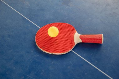 Kırmızı masa tenisi raketi, aralarında sarı bir top, mavi arka planda, ping pong spor ekipmanları, masanın ortasına ilişkin simetri konsepti, beyaz bir çizgi, üst görüş.,