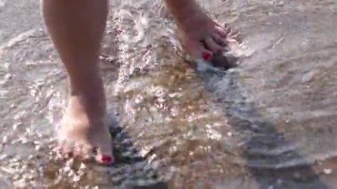 Çıplak ayaklı, kırmızı pedikürlü, kumlu bir sahilde köpüklü su dalgaları içinde, kadın ayaklarının en üst görüntüsü, kumsalda ayaklarını ılık deniz suyunda ıslatan, deniz kenarında kaygısız bir tatil.,