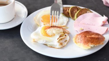 Tanımlanamayan bir kadın, beyaz tabakta çörek yerken çöreği yumuşak sarıya batırıyor, yaz tatilinde otel restoranında güneşli bir günde terasta protein ile geleneksel İngiliz kahvaltısı yapıyor.,
