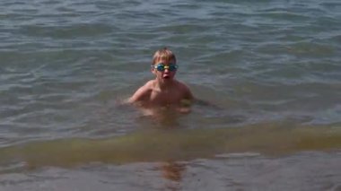 8 yaşındaki yüzme gözlüklü bir çocuk mavi denizin kumlu sahilinde uzanır, yaz tatillerinde yüzmeyi sever, güneşli bir günde ferahlatıcı yüzmeyi sever.