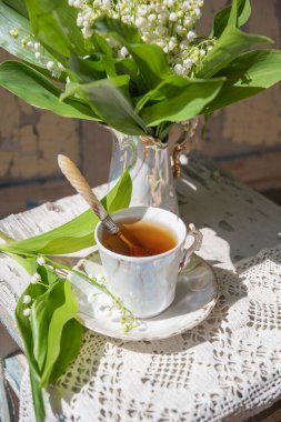 Kahvaltınla rahat bir hayat, antika bir porselen fincanda sıcak çay ve antika bir vazoda bir buket zambak.,