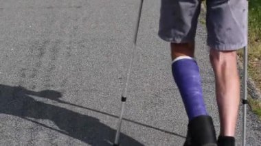 Modern mavi fiberglas alçılı sol bacağı kırık bir adam yürüyüş ayakkabılarıyla yürür, koltuk değnekleriyle yürür, yaralı bacağı yukarıda tutar, stresten korur, rehabilitasyon konseptini korur.,