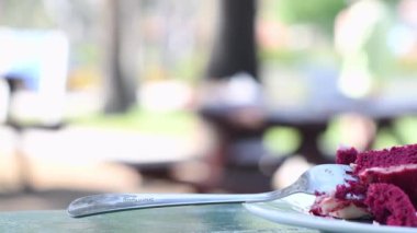 Masadaki beyaz bir tabakta taze böğürtlenlerle süslenmiş yenmemiş kırmızı kadife pasta ve geleneksel bir Armudu bardağında bir fincan Türk çayı. Arka planda bulanık bir şekilde yürüyen insanlar.,