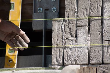 Duvardaki tuğlaları seviyeyle hizalayan kişi, arka plandaki araçlar, inşaat işindeki hassasiyet kavramı,