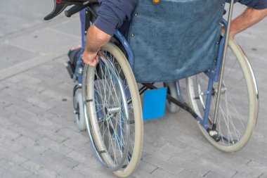 Tekerlekli sandalyede oturan tanınmayan bir adam teras boyunca yürür, elleriyle tekerlekleri çevirerek hareketini yönetir, engelliler için aktif yaşam kavramı ve olası hareket şekilleri,