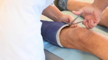 Klinikteki hemşire hastalara makas kullanarak güçlü fiberglas kesiyor. Talimatlara göre önlem alıyor, hasta sessizce oturuyor, profesyonel yardım kavramı.,