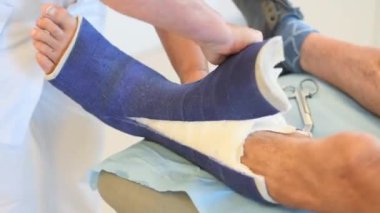 Klinikteki hemşire talimatlara göre hastanın bacağından güçlü fiberglas çıkartıyor, önlem alıyor, hasta sessizce oturuyor, profesyonel bakım konsepti...,