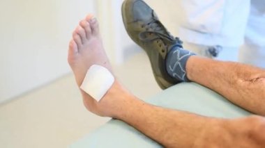Klinikteki hemşire talimatları takip ederek hastaların bacağındaki bandı dikkatlice çıkarıyor, önlem alıyor, profesyonel bakım kavramı uyguluyor.,