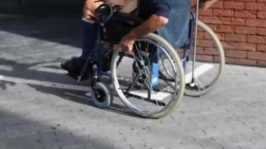 Tekerlekli sandalyedeki kişi, asfalt zeminde yürüyor, elleriyle dönen tekerlekler, hareket kabiliyeti ve bağımsızlığı vurguluyor, dikiz aynası.,