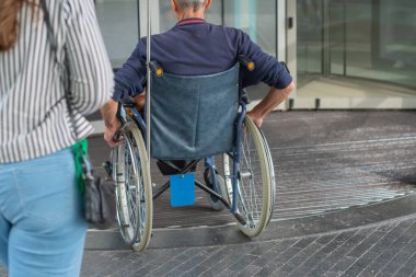 Tekerlekli sandalyedeki adam özel döner kapılı binaya giriyor, hareket özgürlüğü kavramı.,
