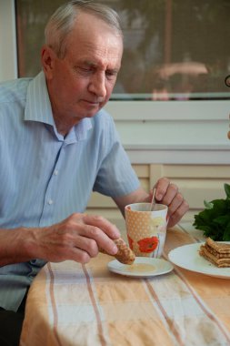 Yaşlı adam gözlemeli çay içiyor, ballı krep yapıyor, geç saatte tatlı kahvaltı yapıyor.,