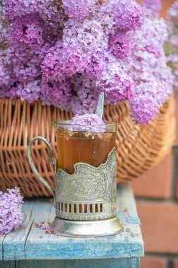 Geleneksel bir Rus çay fincanında leylak çiçekleriyle dolu bir sepet dolusu leylak çiçeğinin yanında duran çay, sıcak bir bahar atmosferi yaratır.