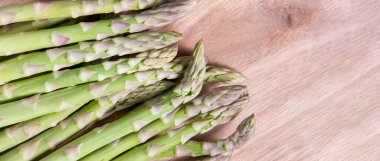 Bir sürü çiğ, kalın yeşil kuşkonmaz sapları, taze, iştah açıcı yeşil sebzeler ahşap arka planda, kopyalama alanı.