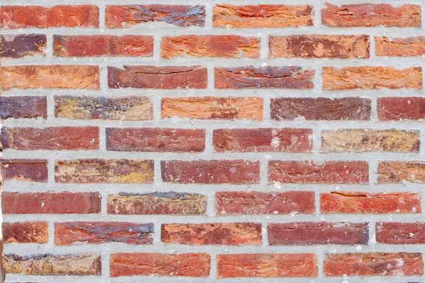 Kırmızı ve kahverenginin farklı tonlarında bir tuğla duvarı, tekrarlayan sedye tuğlaları deseni, kırsal tarzda çekici desenli arka plan.
