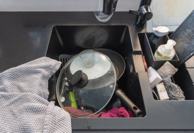 Kirli bulaşık yığını, tencere, kap kacak, mutfak lavabosunda yıkanmayı bekliyor, ihmal edilmiş işleri ve yoğun bir yaşam tarzını sembolize ediyor.