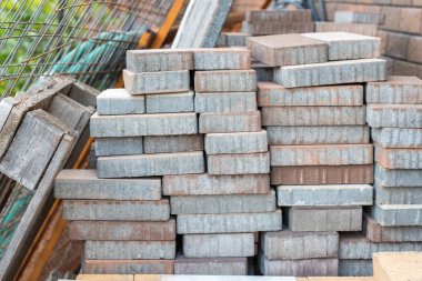 Gri ve kırmızımsı beton kaldırım taşları tomar tomar, bahçe yolları, garaj yolları ve çeşitli dış döşemeler inşa etmeye ve yerleştirmeye hazır konut veya ticari ortamlarda