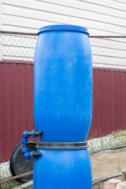 Mavi plastik yağmur fıçıları borulara yığılmış ve bağlanmış, bunu kendiniz için bir yağmur suyu hasat sistemi oluşturarak verimli açık hava sulama ve sürdürülebilir peyzaj uygulamalarını teşvik etmek için