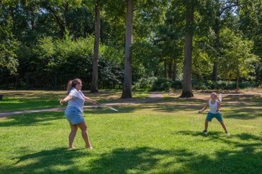 Mother and son playing badminton on a sunny day in a green park, enjoying their leisure time, engaging in family sport, and having fun together outdoors during summer