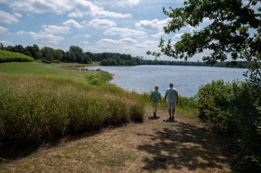 Elderly couple walks hand in hand towards a peaceful lake on a sunny summer day, enjoying a relaxing outdoor activity and a healthy, active retirement life together