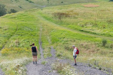 Couple of hikers navigating a challenging dusty trail on a grassy hillside, enjoying a healthy and active lifestyle while trekking through the vast, open natural landscape under a bright summer sky