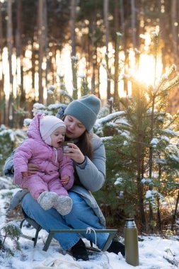 Anne ve bebek, karlı bir ormanda termostan sıcak çayın keyfini çıkarıyorlar.