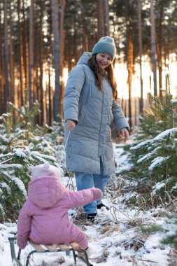 Anne gün batımında küçük kızını karlı bir ormanda kızağa çekiyor..