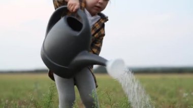 Küçük kız büyük bir su bidonuyla tarlayı suluyor.