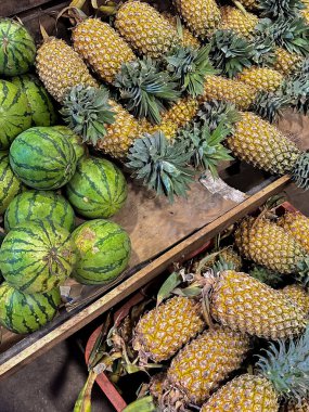Yerel bir markette ahşap raflarda sergilenen taze ananas ve karpuzlar..