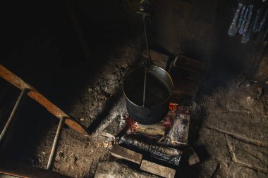 Water is heated in an old cauldron on fire, in an old rural room