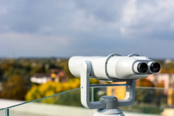 Large, stationary observation binoculars mounted on the observation deck. The binoculars are mounted on a solid, rotating column. Photo taken in natural, soft light.