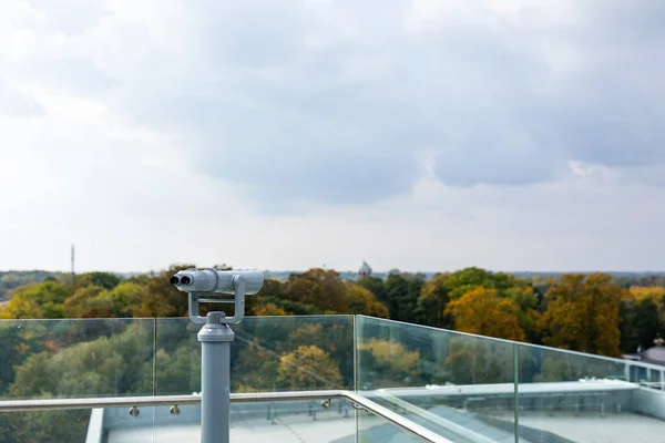 Large, stationary observation binoculars mounted on the observation deck. The binoculars are mounted on a solid, rotating column. Photo taken in natural, soft light.