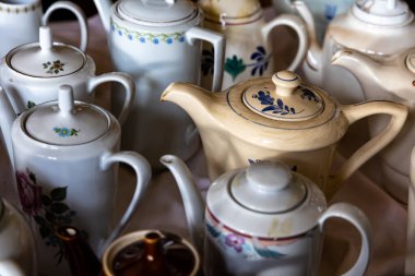 Bit pazarında antika seramik, porselen çay ve kahve demliği koleksiyonu. Fotoğraf içeride doğal, düşük ışıkla çekildi.