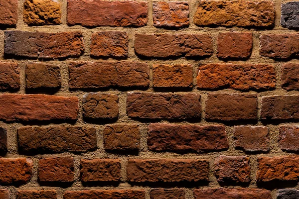 A red brick wall illuminated at night. Surface texture emphasized by the angle of incidence of light