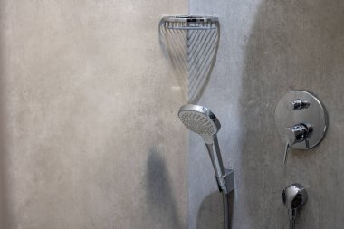 Duş tepsisinin duvarına monte edilmiş gri seramik fayanslarla bitirilmiş bir duş başlığı. Sabunu tutmak için rafın yanında.