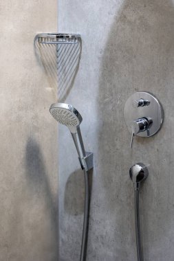 Duş tepsisinin duvarına monte edilmiş gri seramik fayanslarla bitirilmiş bir duş başlığı. Sabunu tutmak için rafın yanında.
