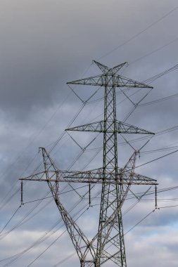 The silhouette of a high-voltage pylon against a dramatically cloudy sky. Development of high-voltage transmission networks
