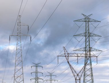 The silhouette of a high-voltage pylon against a dramatically cloudy sky. Development of high-voltage transmission networks