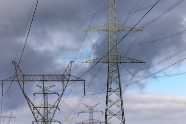 The silhouette of a high-voltage pylon against a dramatically cloudy sky. Development of high-voltage transmission networks