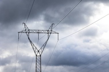 The silhouette of a high-voltage pylon against a dramatically cloudy sky. Development of high-voltage transmission networks