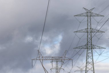 The silhouette of a high-voltage pylon against a dramatically cloudy sky. Development of high-voltage transmission networks
