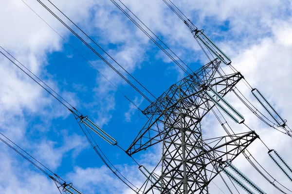 High-voltage pylon against a blue sky with a slight cloud cover. High voltage transmission lines silhouette