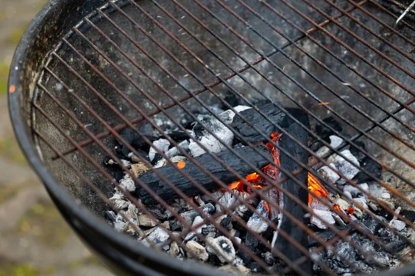 Hearth of a metal grill with glowing charcoal flame. Preparation for barbecue in the garden.