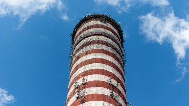 Uzun bir elektrik santralinin bacasına yerleştirilmiş bir cep telefonu anteni. Güneşli bir günde mavi gökyüzüne karşı bir nesne.