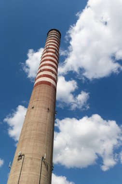 Uzun bir elektrik santrali bacasına yerleştirilmiş bir cep telefonu anteni. Güneşli bir günde mavi gökyüzüne karşı bir nesne.