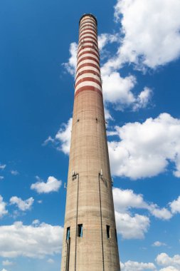 Uzun bir elektrik santrali bacasına yerleştirilmiş bir cep telefonu anteni. Güneşli bir günde mavi gökyüzüne karşı bir nesne.