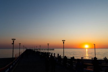 Gün batımında iskelede bir sürü insan olur. Bulutsuz bir akşamda çekilen statik çekim       