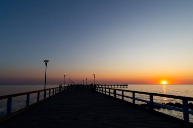 Gün batımında iskelede bir sürü insan olur. Bulutsuz bir akşamda çekilen statik çekim       