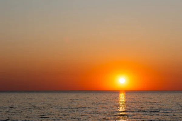 穏やかな海の上に大きなオレンジ色の太陽が沈む 雲のない夜の間に撮影された静的ショット ストック画像