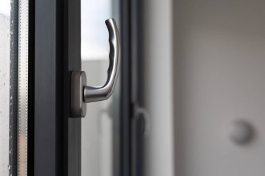 Kamu binasındaki büyük bir pencerenin kolunu eğ ve çevir. Pencere plastik, görünür silikon mühürlerden yapılmış..