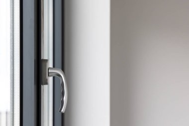 Kamu binasındaki büyük bir pencerenin kolunu eğ ve çevir. Pencere plastik, görünür silikon mühürlerden yapılmış..